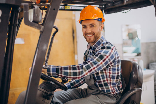 Hombre con casco de seguridad naranja sonriendo mientras conduce un montacargas en un entorno industrial