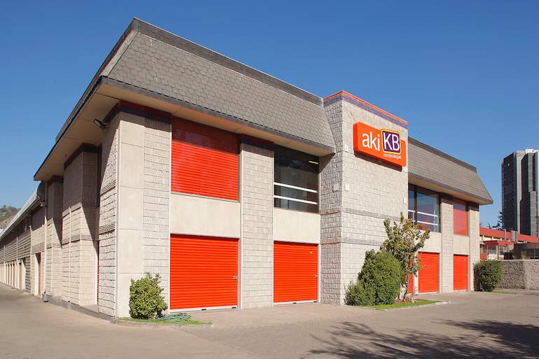 Edificio de almacenamiento con portones enrollables rojos y letrero de akiKB bajo un cielo despejado