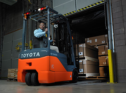 Operador conduciendo un montacargas Toyota naranja y gris para cargar cajas en un camión en un muelle de carga. En representacion del trabajo realizado en Agroexportadora San José